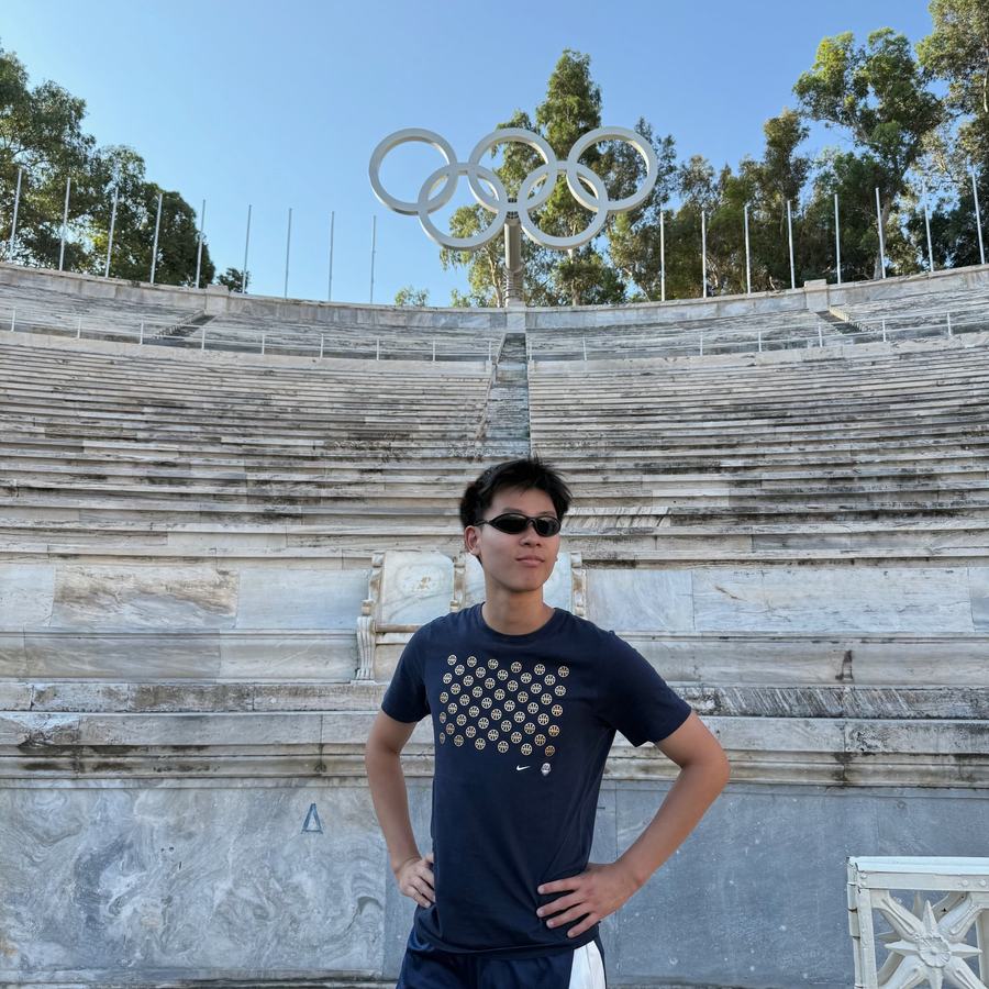 Ethan standing hands on hips in the marble Panathenaic Stadium under the Olympic rings