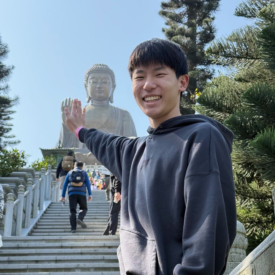 Ethan waving in front of the giant Tian Tan Buddha statue at the top of a long stairway