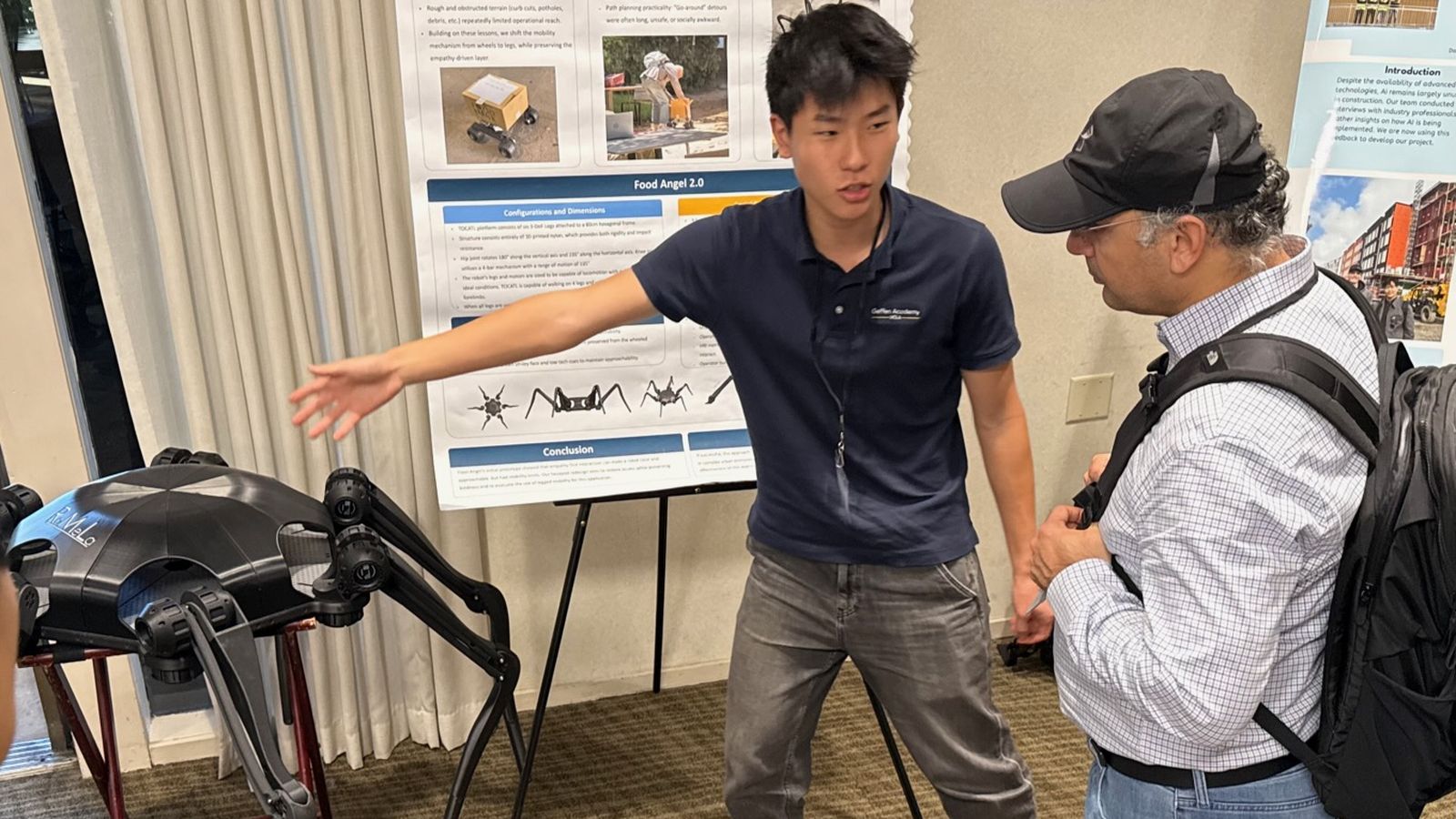 Ethan explaining his hexapod research poster to a visitor, with the robot beside him