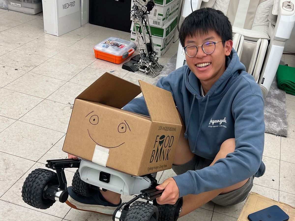 Ethan sitting on the lab floor, smiling, holding Food Angel with its box open