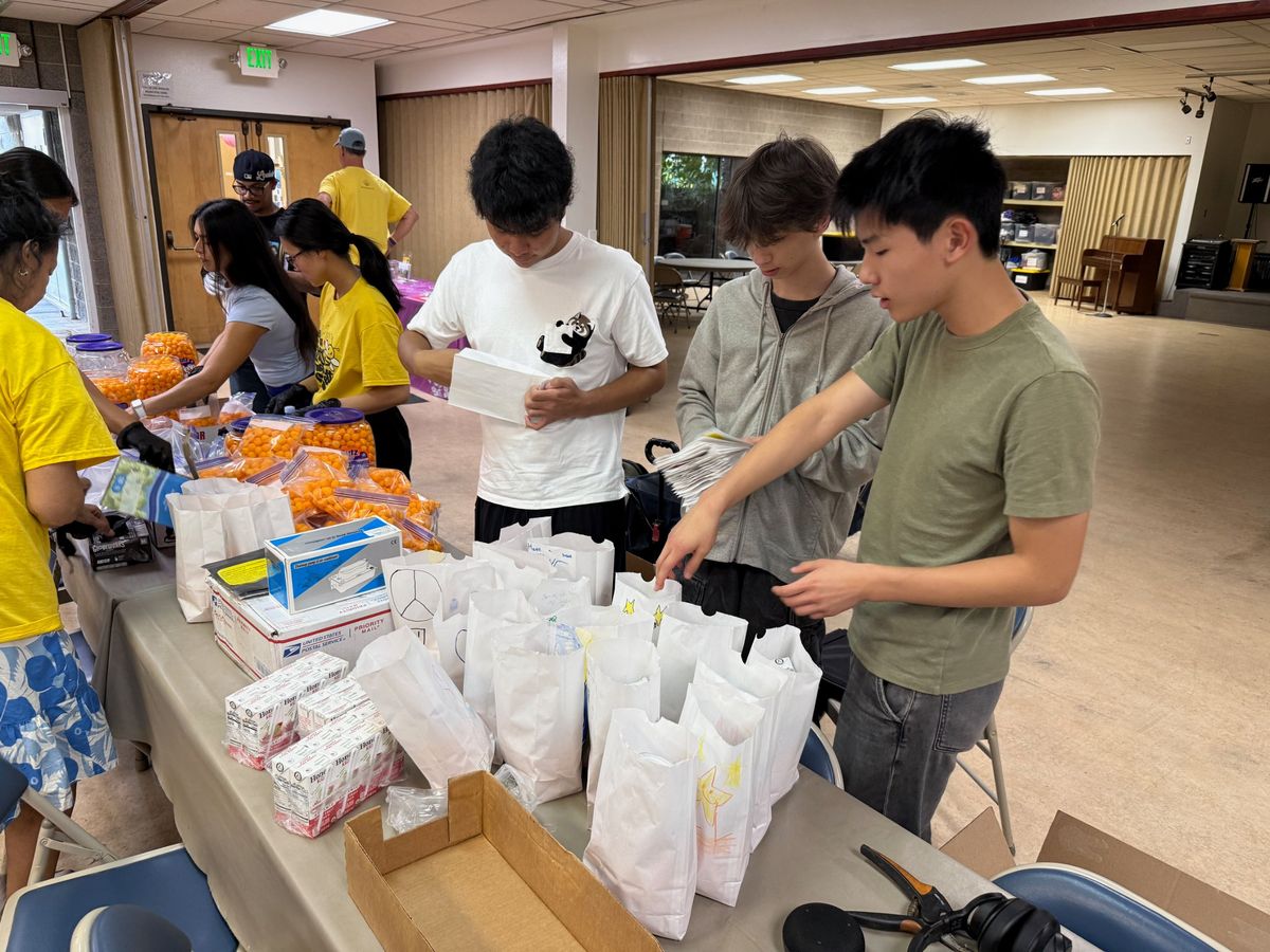 Ethan and two friends packing meals into paper bags at a community center
