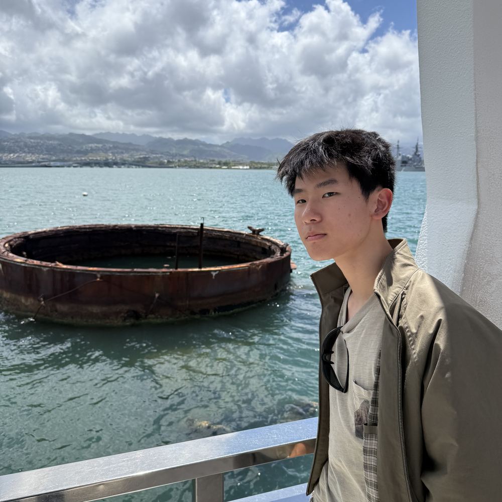 Ethan at the USS Arizona Memorial, with the rusted gun turret base of the sunken battleship in the water behind him
