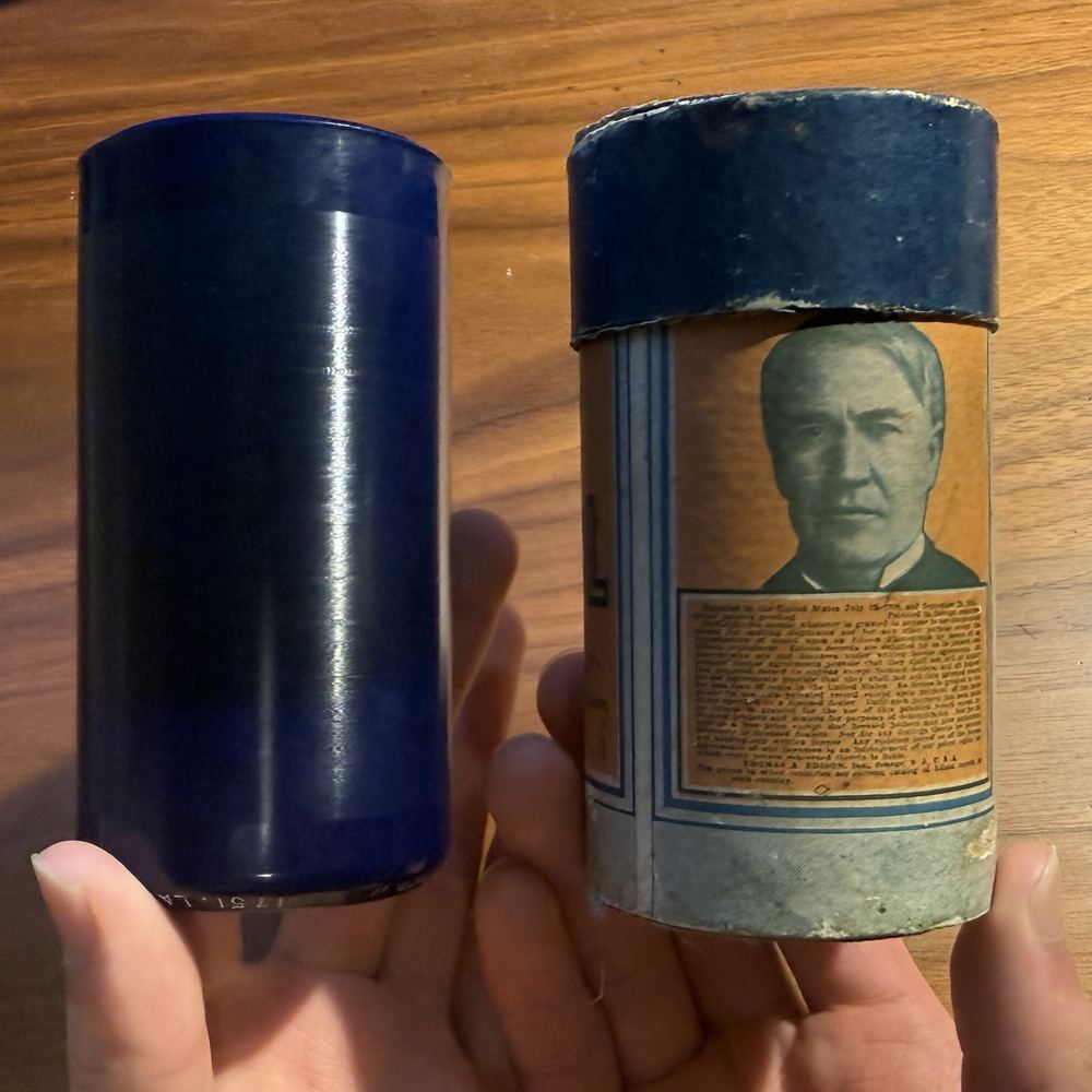 Two old Edison phonograph cylinder containers, one with a portrait of Thomas Edison on the label