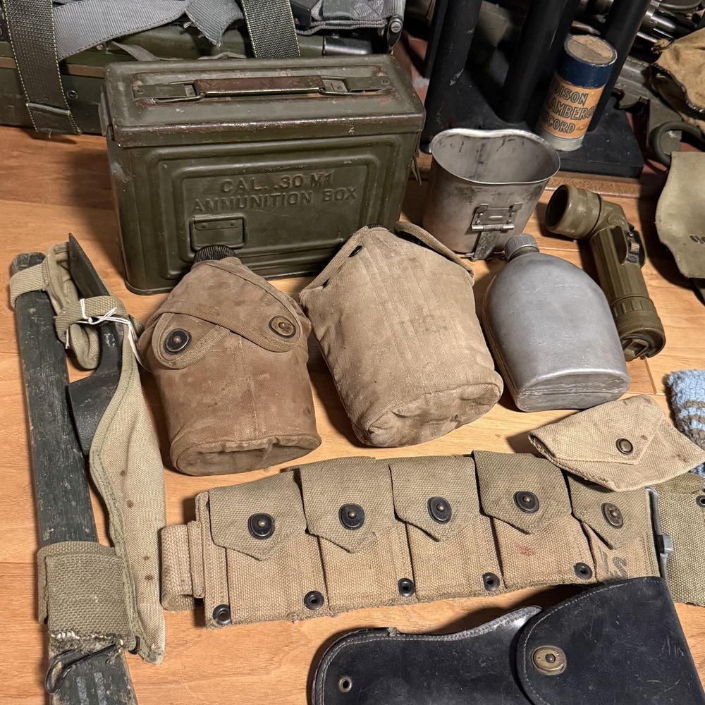 Military field gear: an ammunition box, canteens with covers, a mess cup, a flashlight, and a cartridge belt