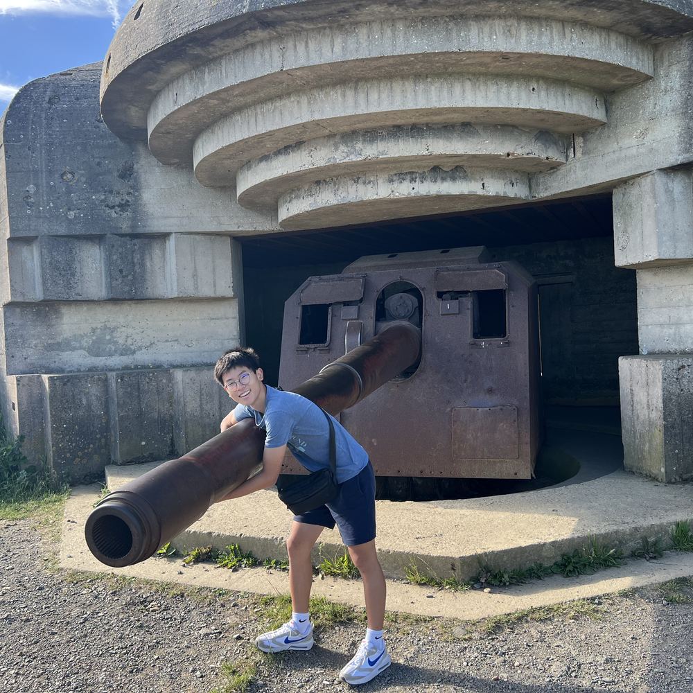 Ethan posing with the barrel of a heavy gun at a concrete coastal bunker in Normandy