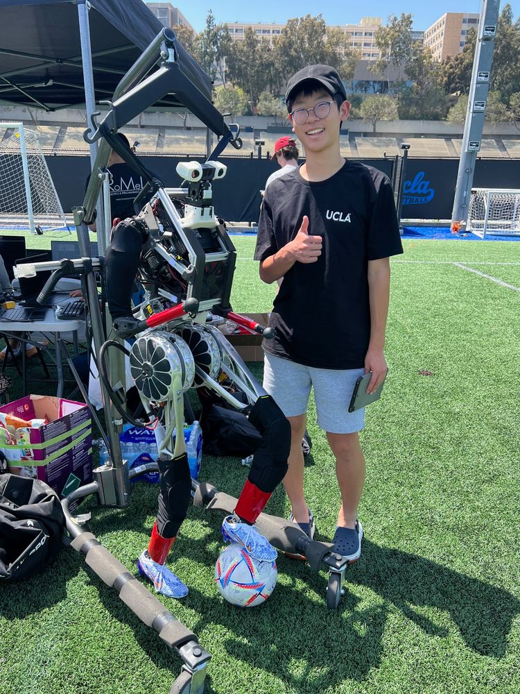 Ethan giving a thumbs-up next to the humanoid robot ARTEMIS on a soccer field at UCLA