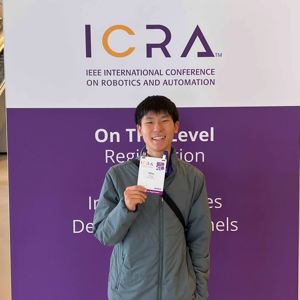 Ethan smiling and holding up his conference badge in front of the ICRA banner