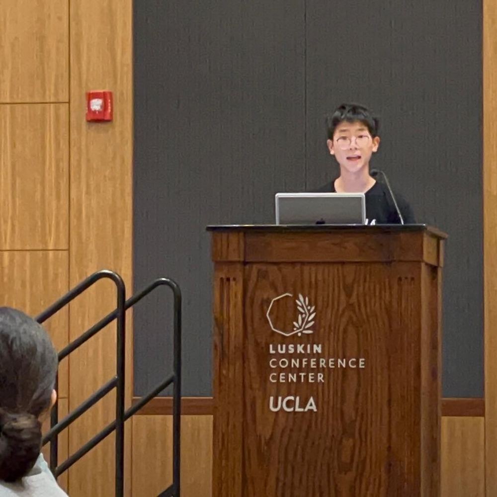 A younger Ethan speaking at a podium at UCLA's Luskin Conference Center