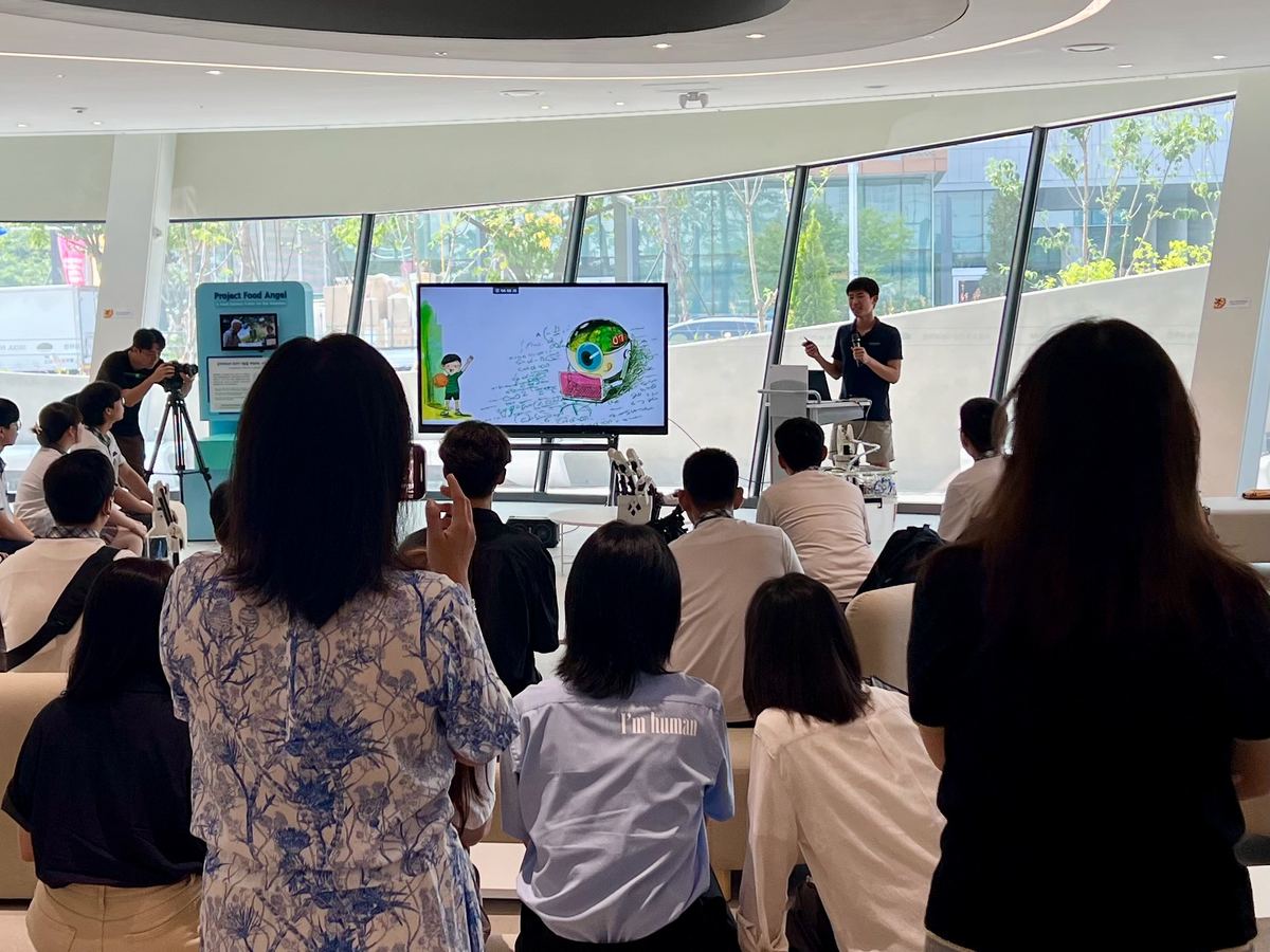 Ethan giving a talk to a seated audience at the Seoul Robot & AI Museum, next to the Food Angel exhibit