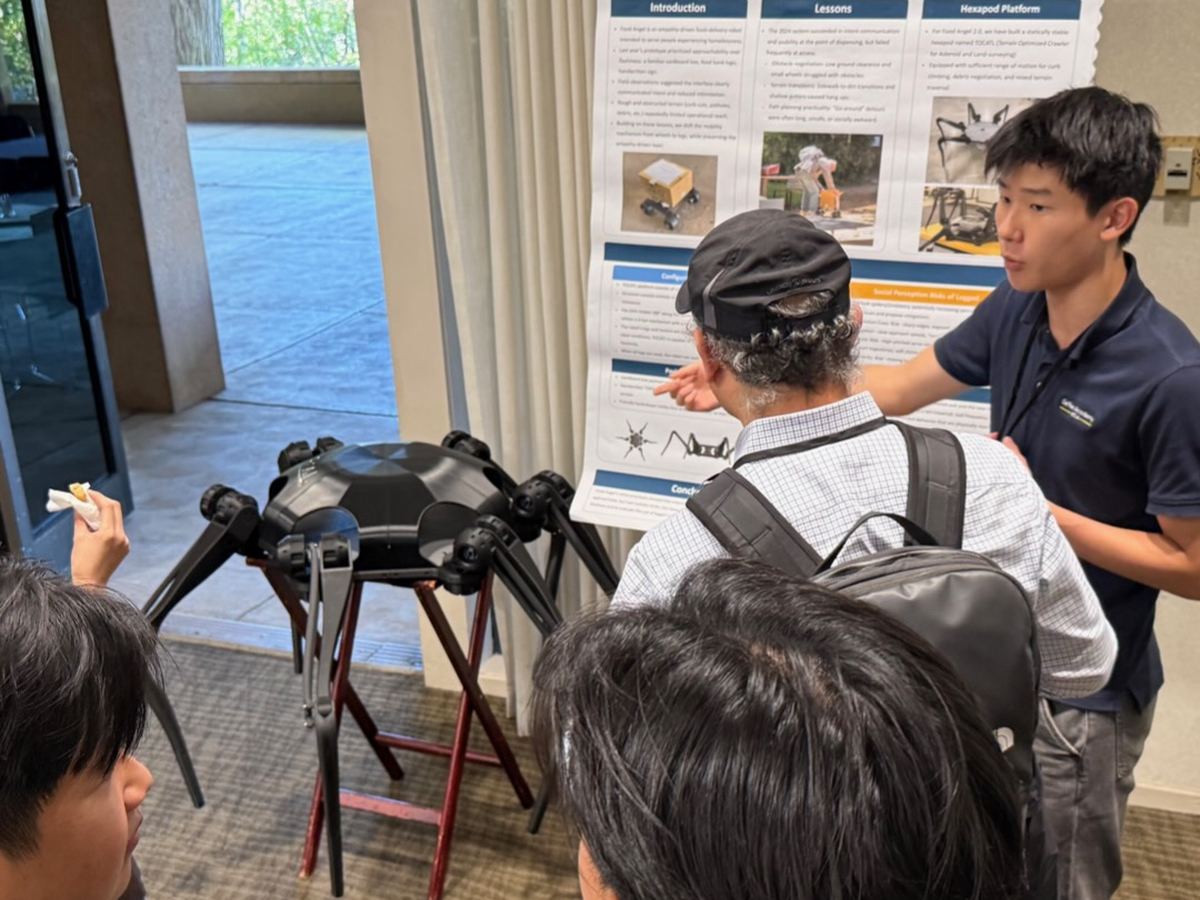 Ethan explaining his hexapod research poster to visitors, with the six-legged robot beside him