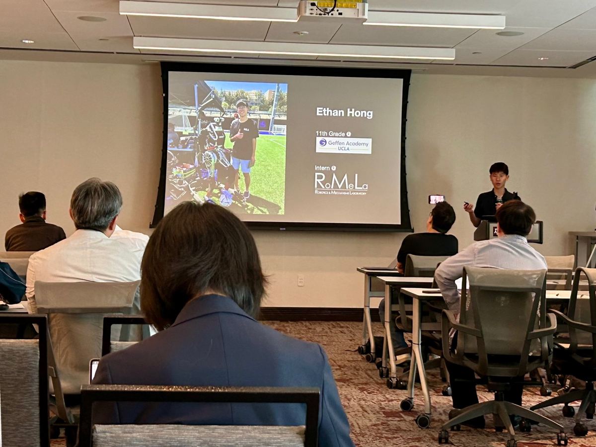 Ethan presenting to a seated audience, with a slide introducing him as an 11th grader at Geffen Academy and an intern at RoMeLa