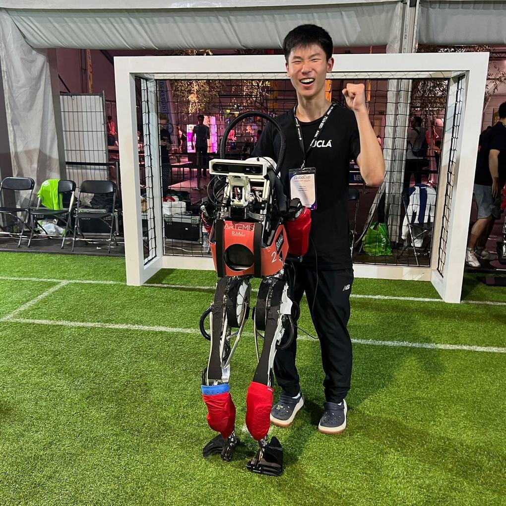 Ethan pumping his fist next to ARTEMIS, robot number 2, in front of a soccer goal at RoboCup 2024