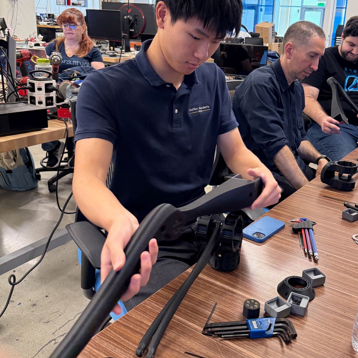 Ethan fitting together the carbon legs of a legged robot at a lab worktable covered in parts and hex keys