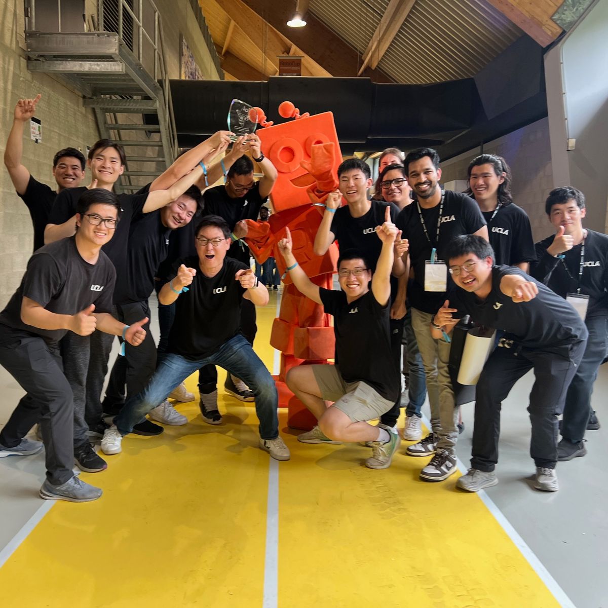 Team RoMeLa in black UCLA shirts celebrating with the championship trophy beside the orange RoboCup mascot