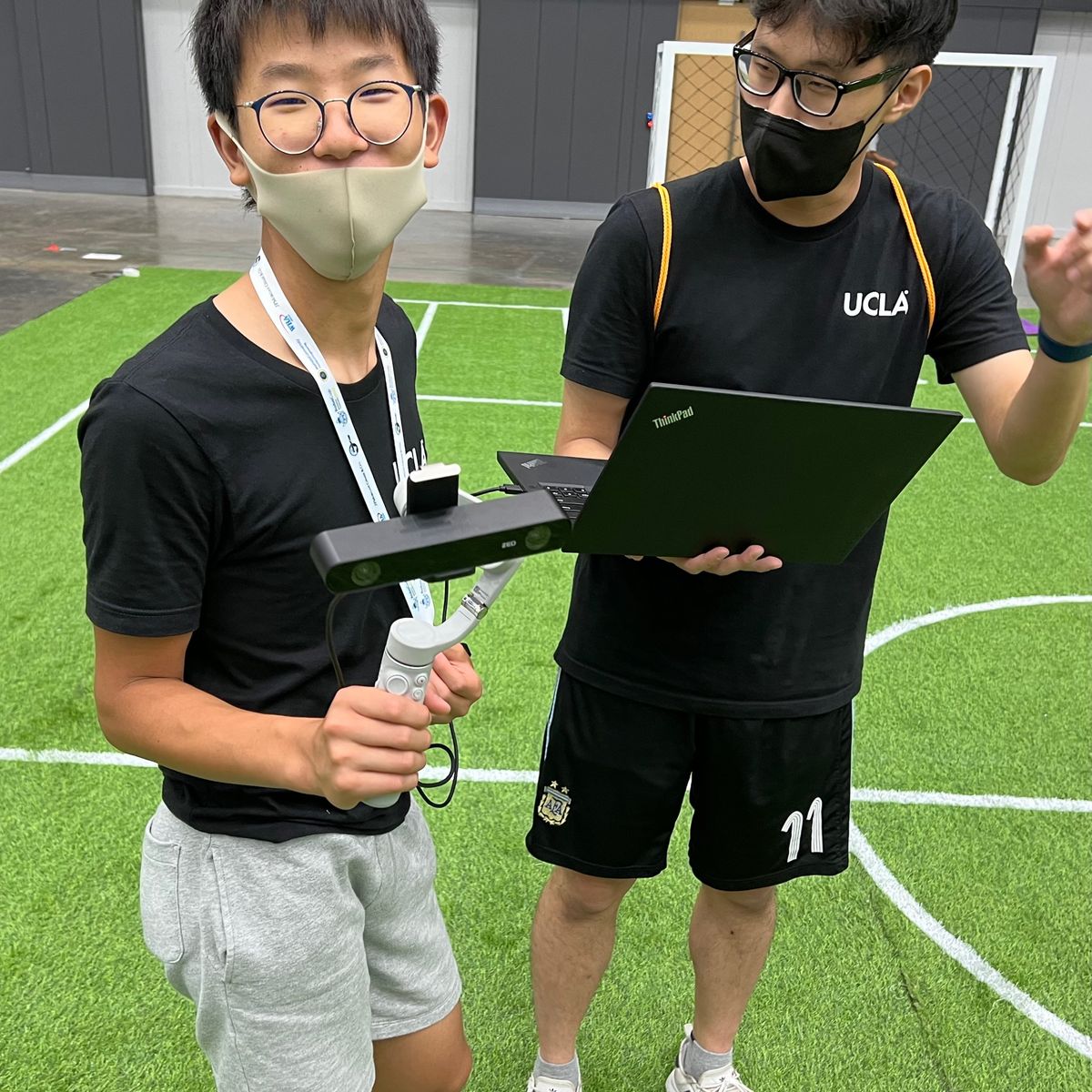 Ethan holding a stereo camera on a gimbal on the soccer field at RoboCup 2022, next to a teammate with a laptop